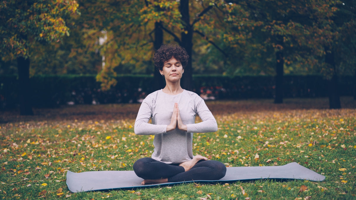Woman meditating in lotus pose on yoga mat outdoors