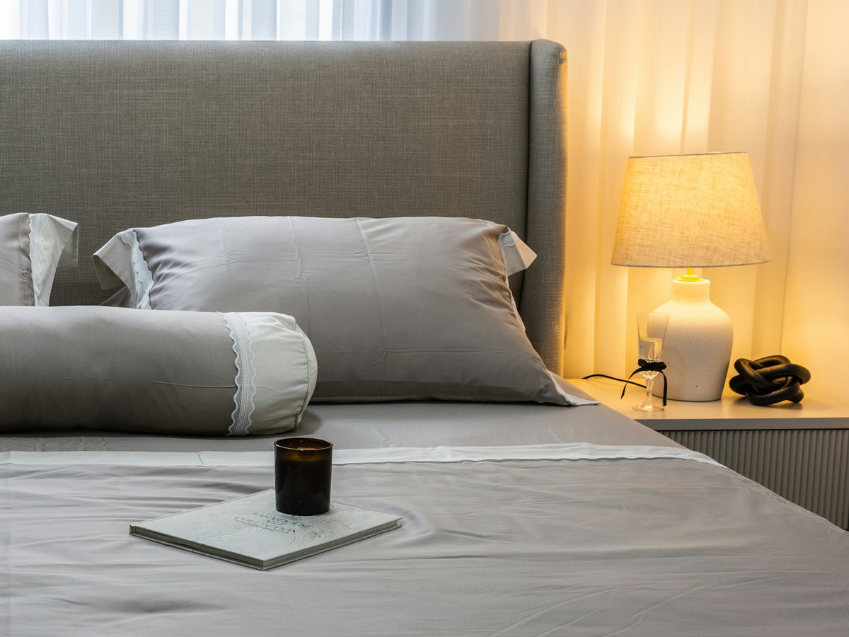 A neatly made bed with grey linens and pillows